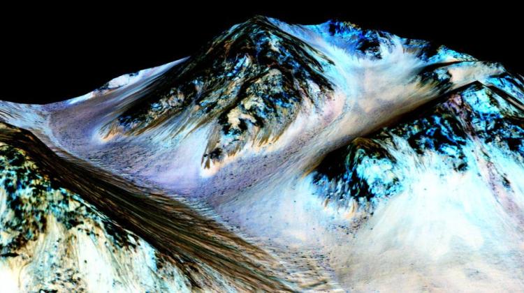 Ciemne, długie na 100 metrów pasma, nazwane „recurring slope lineae” (RSL), okresowo spływają w dół wzgórz na Marsie i wygląda na to, że zostały utworzone przez wodę współcześnie występującą na planecie, gdyż występują tam uwodnione sole. Źródło: NASA/JPL/University of Arizona. 
