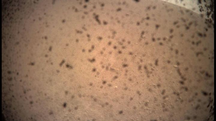 Pierwsze zdjęcie przesłane przez sondę InSight po wylądowaniu na powierzchni Marsa. Zostało wykonane przez osłonę przed pyłem, dlatego widok jest rozmazany i zabrudzony. Źródło: NASA/JPL-Caltech